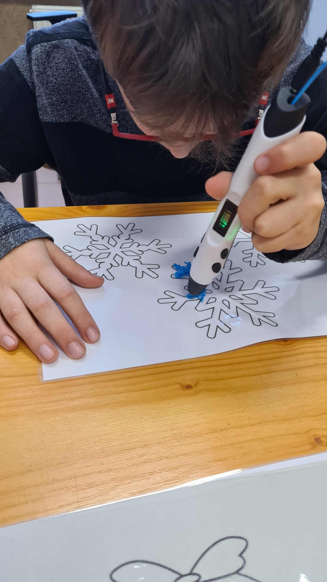 Chłopiec  trzyma w ręku długopis 3d , obrysowuje szablon płatka śniegu.