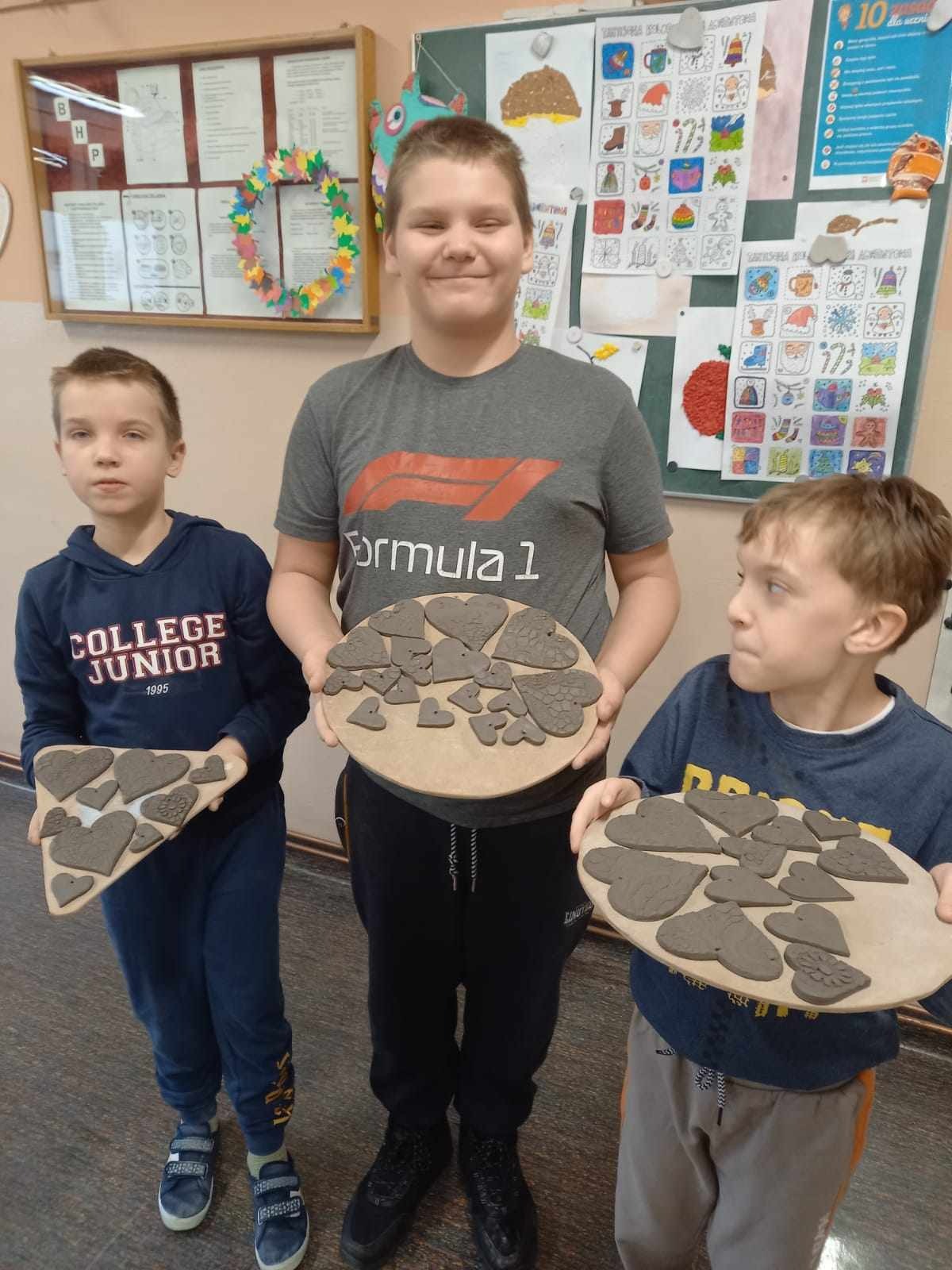 3 uczniów trzyma w rękach patery, na których leżą ceramiczne figurki w kształcie serduszek.