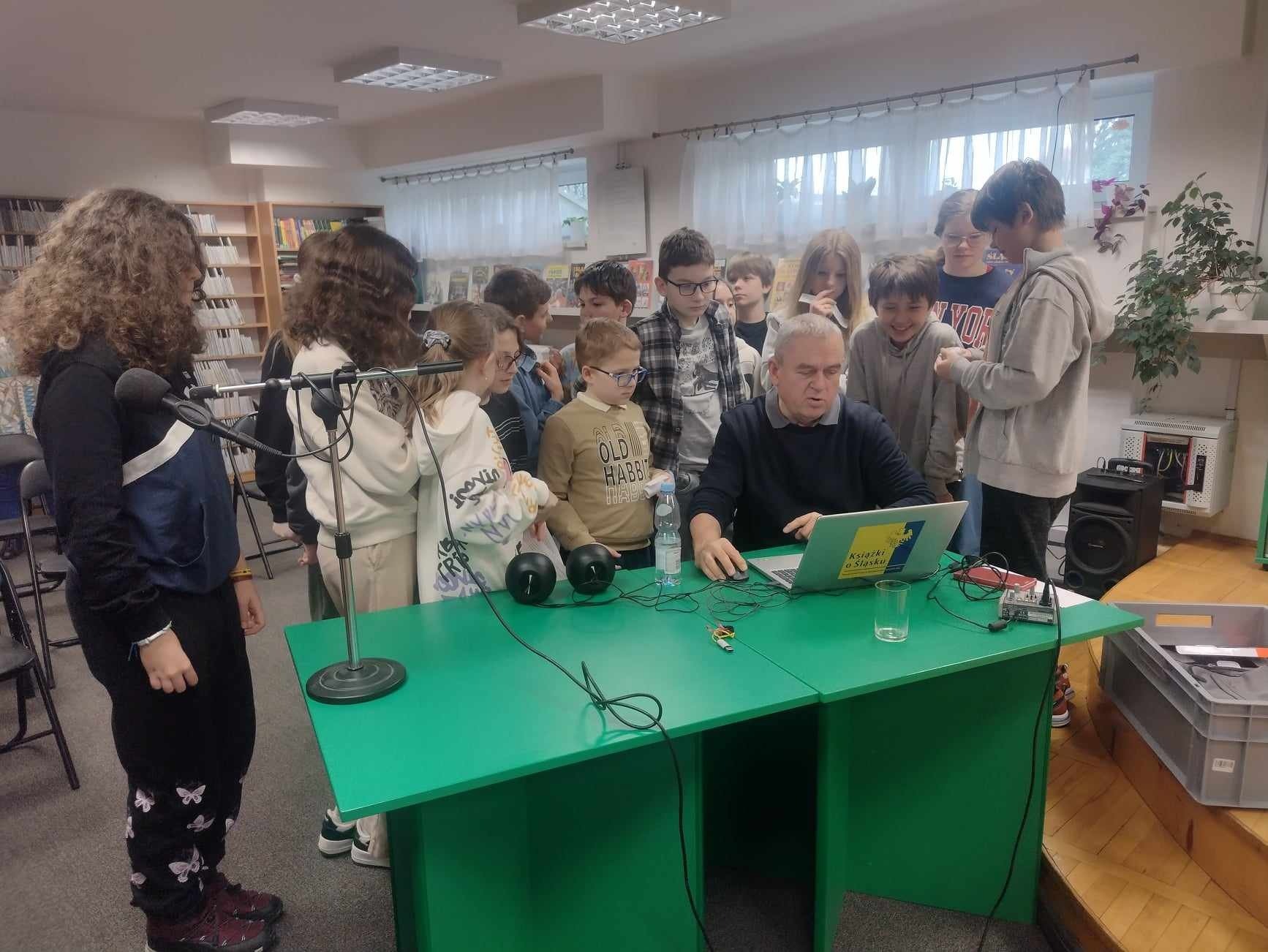 Uczniowie przy biurku prowadzącego wpatrzeni w ekran