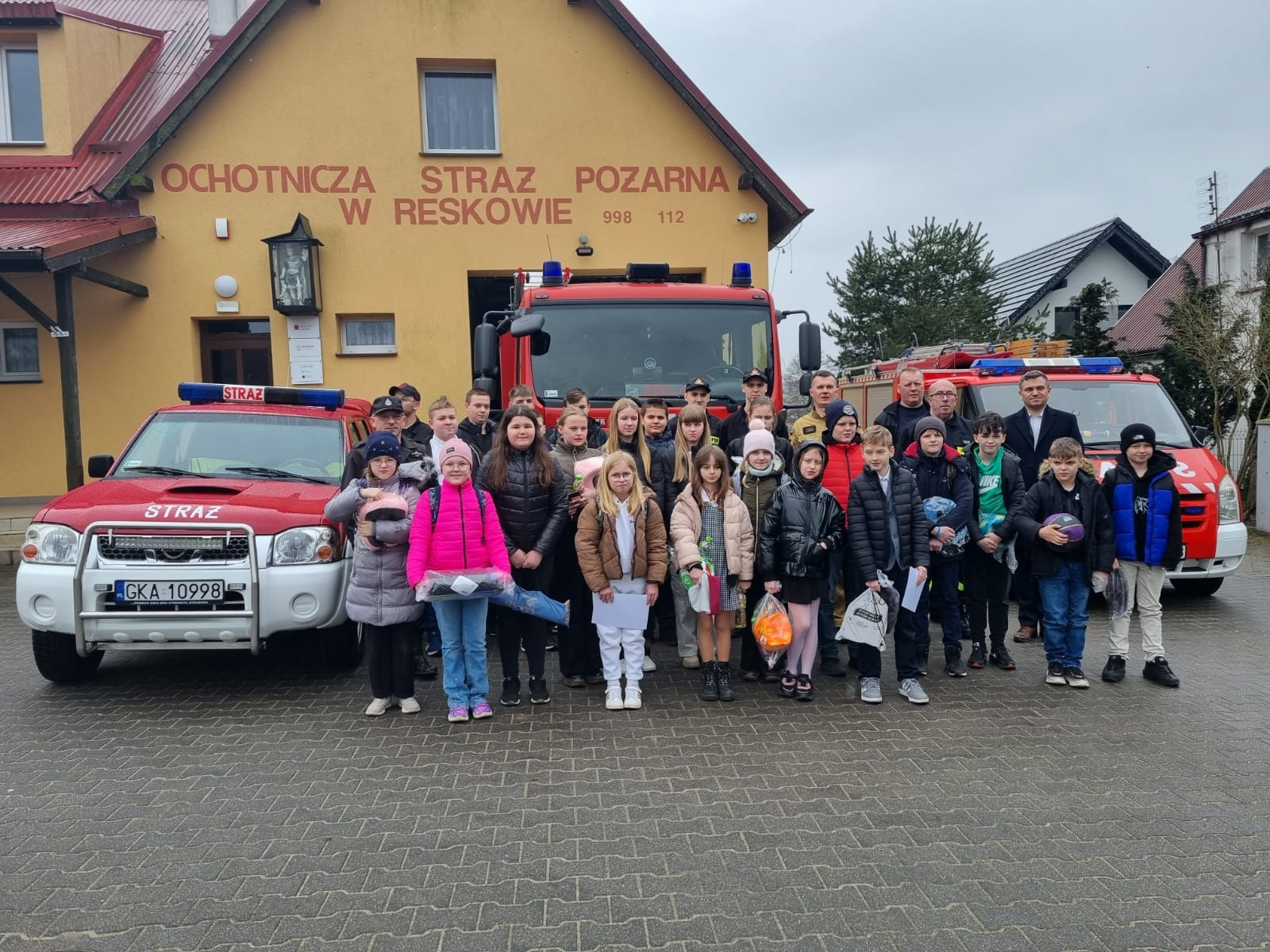 Dzieci  pozują do zdjęcia przy Ochotniczej Straży Pożarnej w Reskowie, towarzyszą im Strażacy oraz Wójt Gminy Chmielno. 