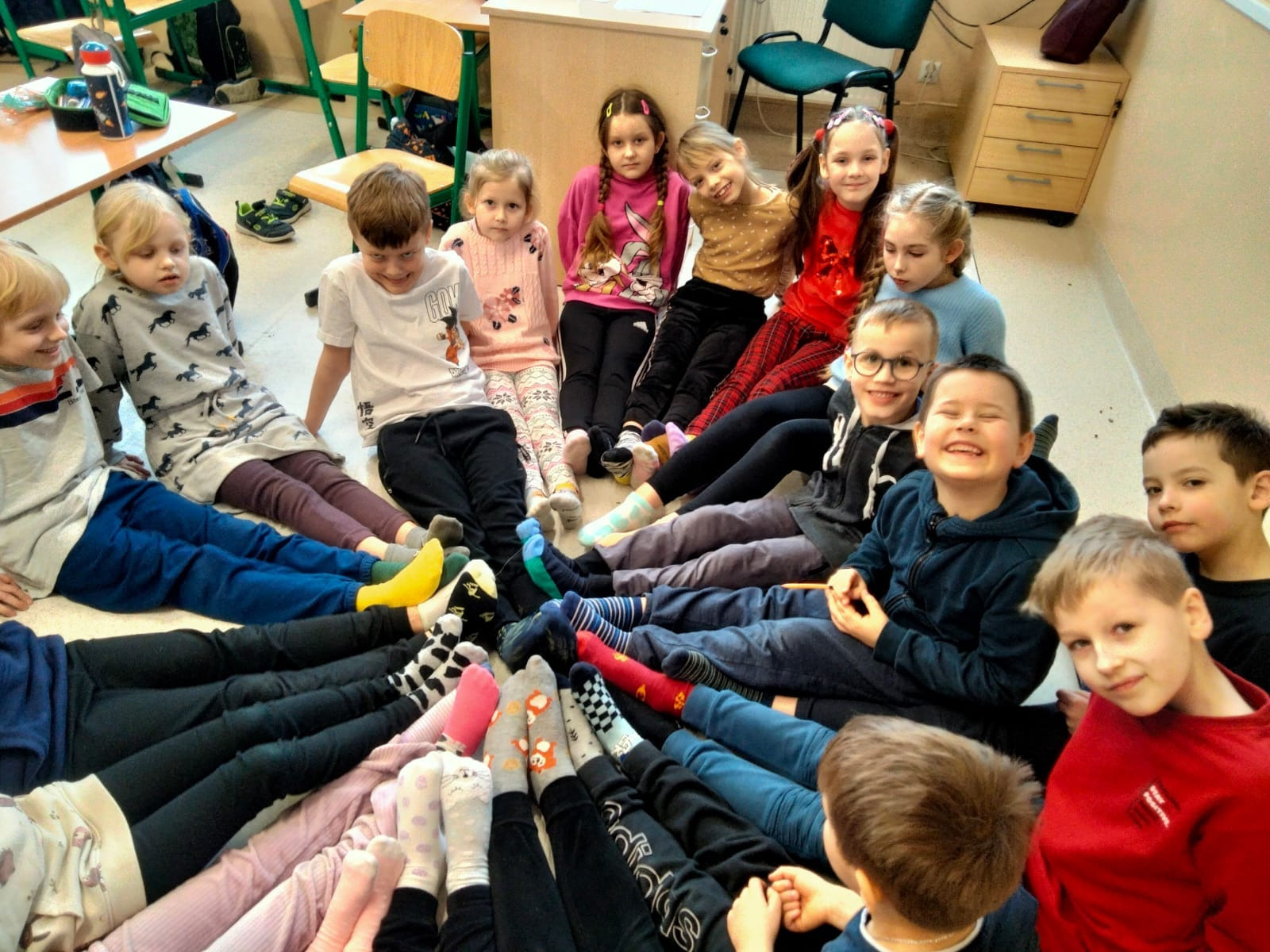Dzieci siedzą w kółeczku i z radością prezentują swoje kolorowe skarpetki. 