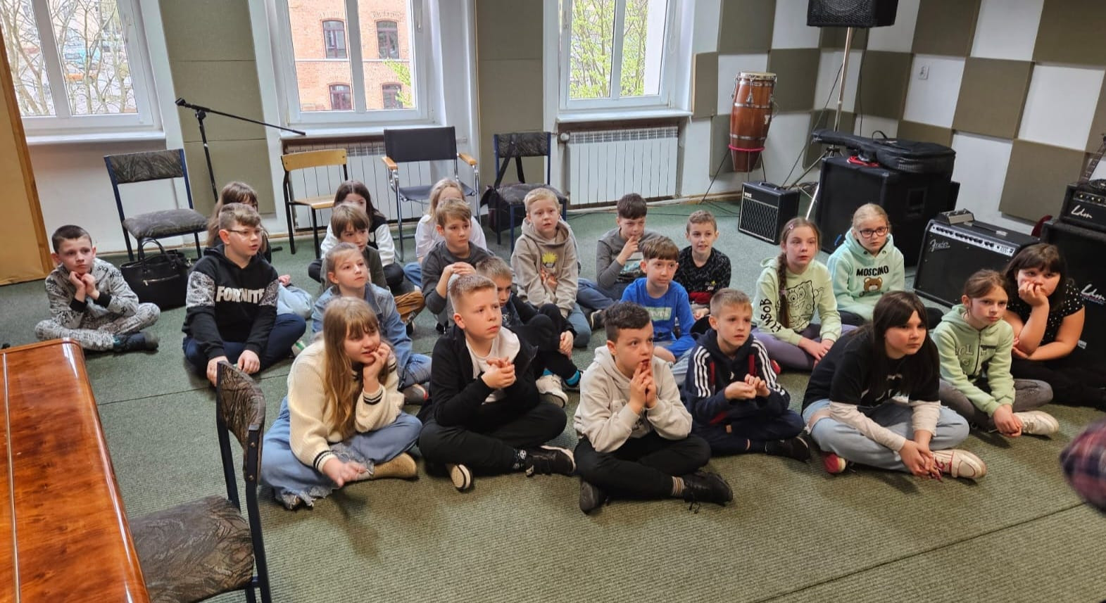 Grupa uczniów siedzi na dywaniku w sali muzycznej MDKu