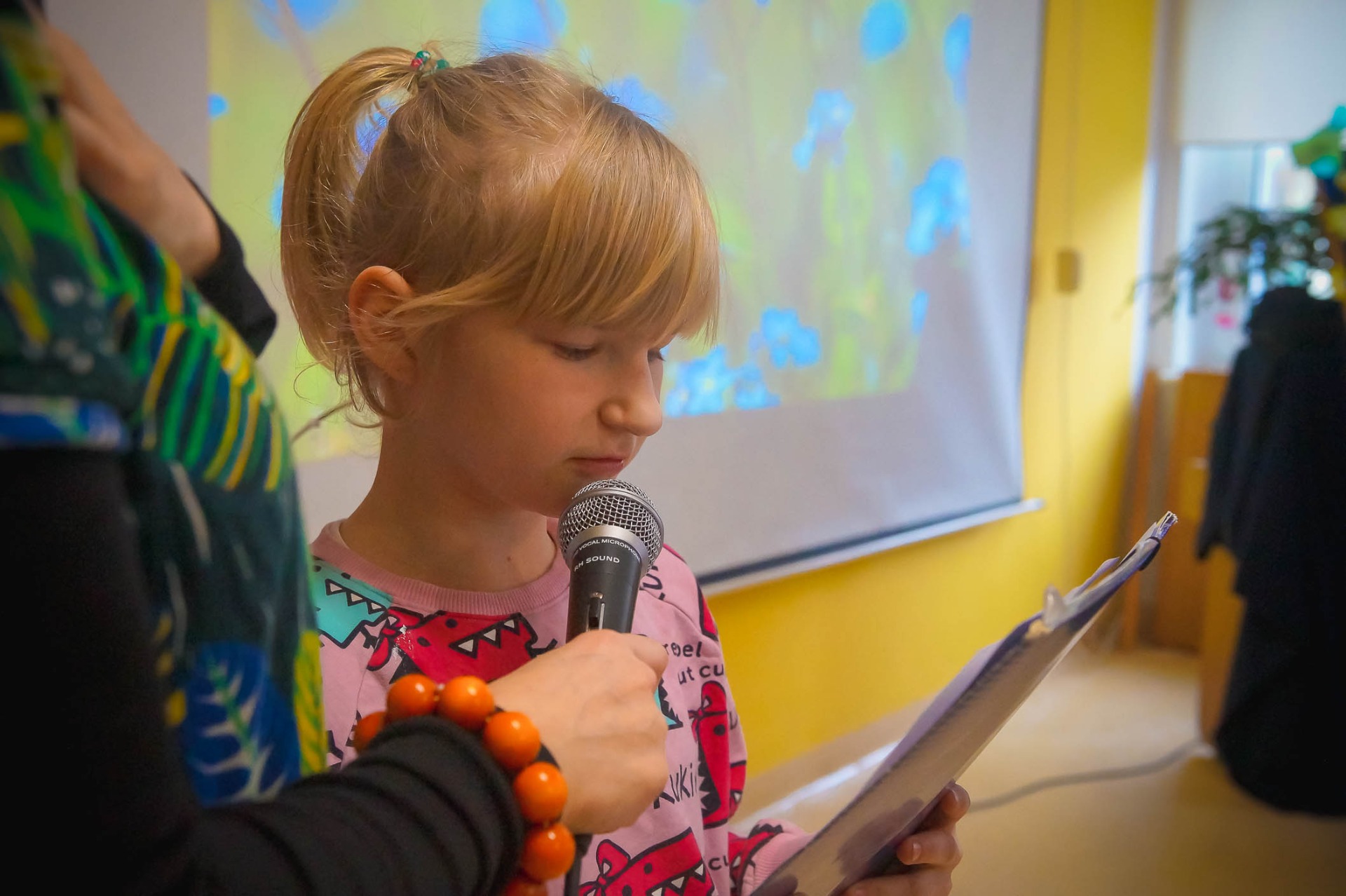 Dziewczynka czyta wiersz, ma do ust przystawiony mikrofon