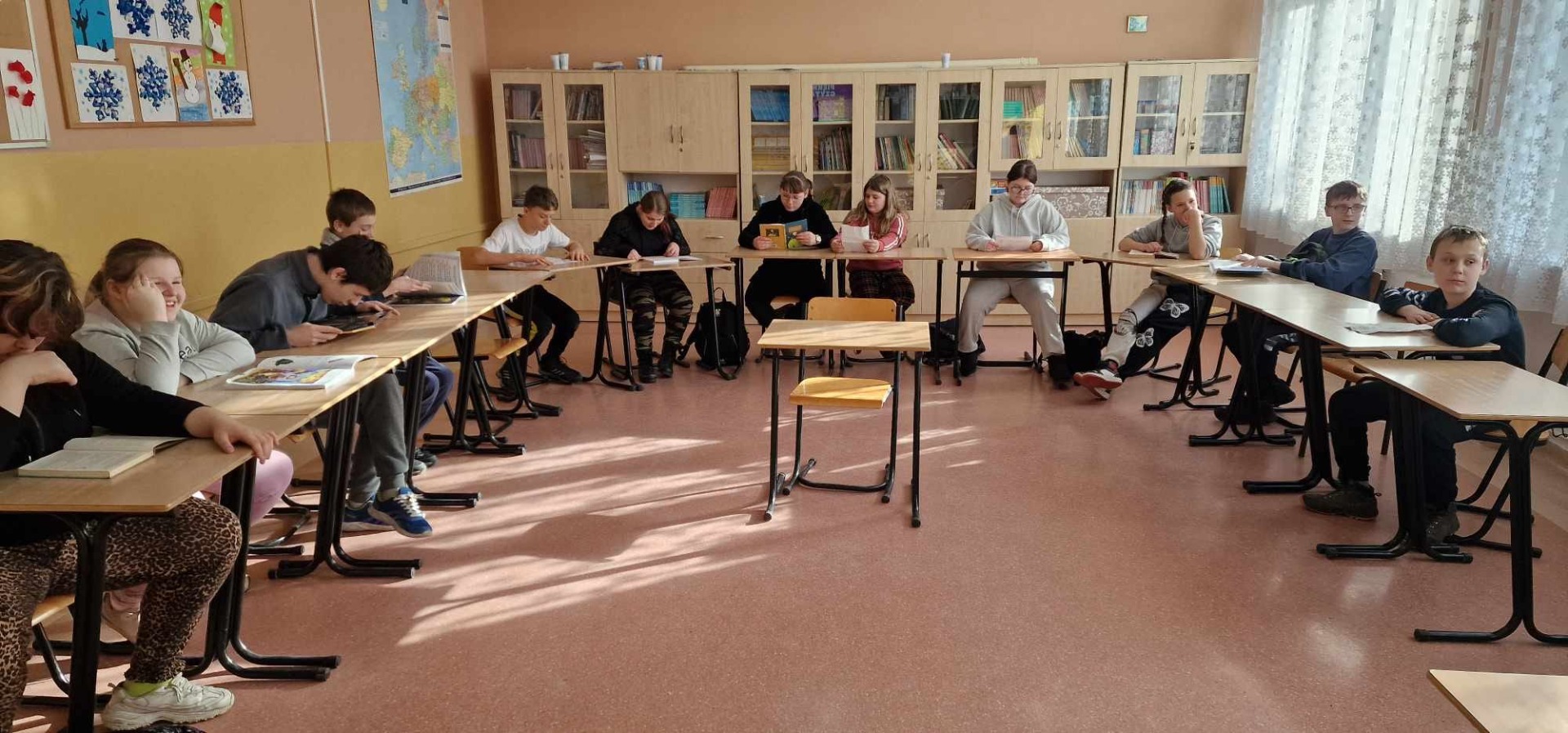 Uczniowie siedzą  przy ławkach ułożonych w kształt litery U