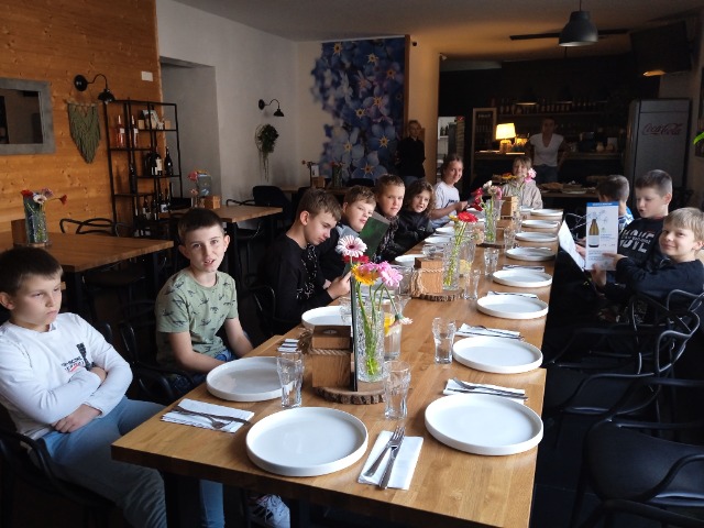 13 uczniów siedzi przy stole w restauracji.