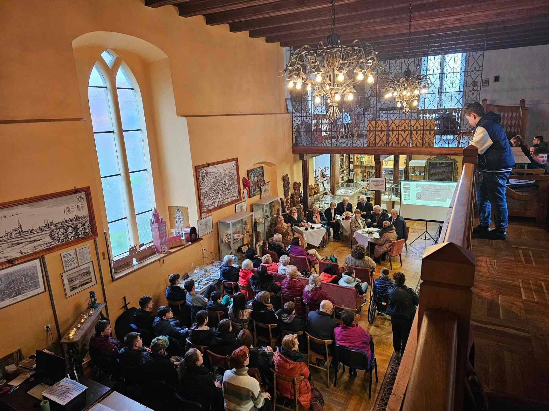 Wnętrze Kaplicy św.Ducha. Zaproszeni goście siedzą na krzesełkach. Przedstawiciele Uniwersytetu Trzeciego Wieku czytają poezję Cz.Miłosza.