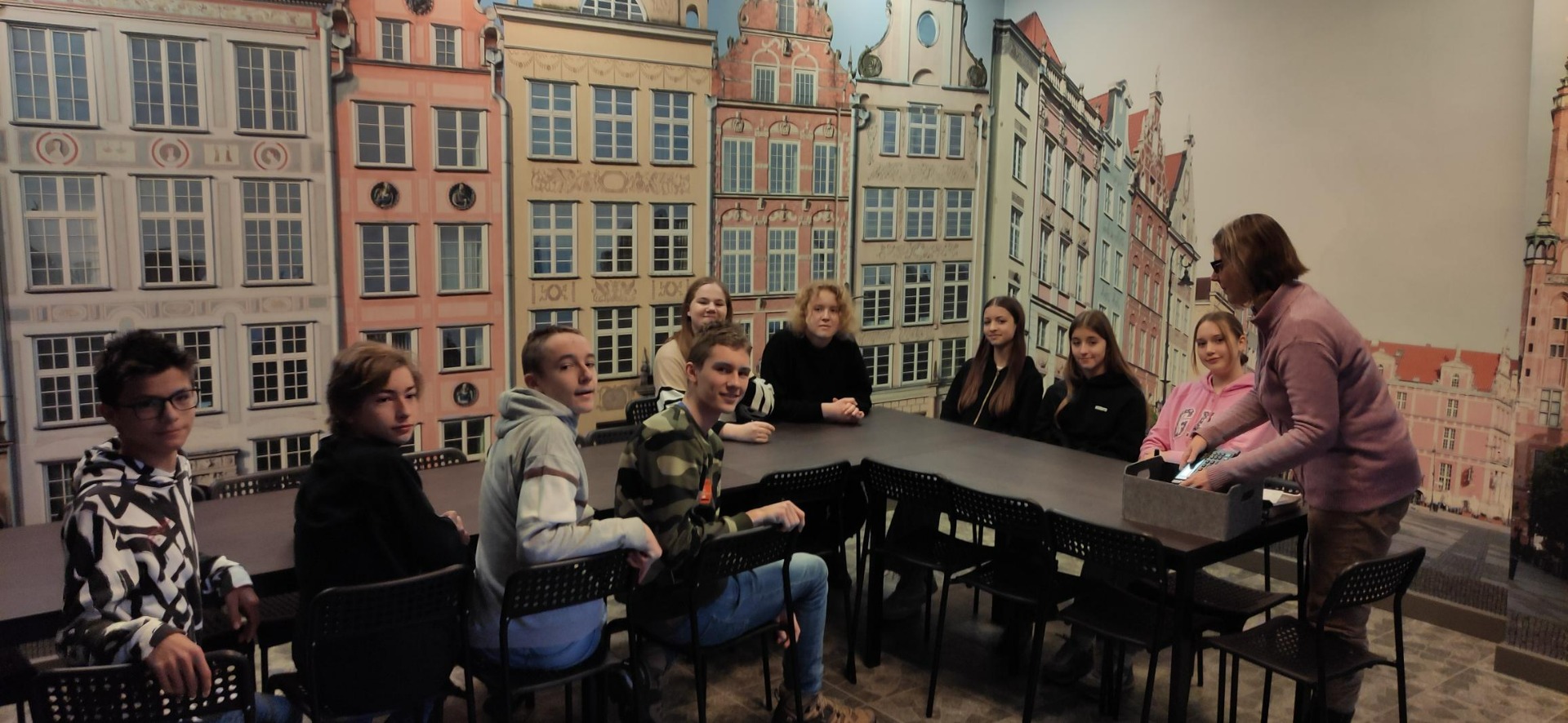 Uczniowie słuchają pani przewodnik w muzeum Niewidzialny Gdańsk. W tle kamieniczki Głównego miasta Gdańsk.