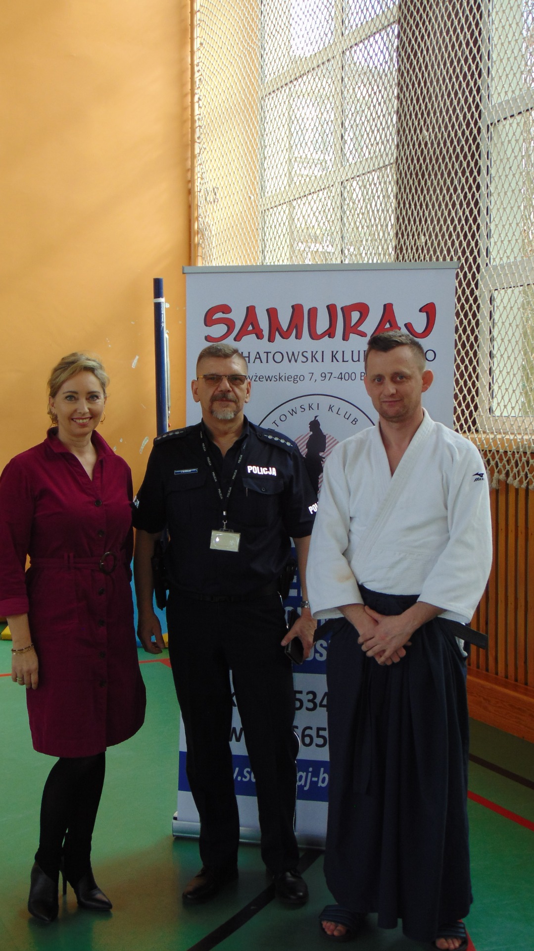 Pani Dyrektor, przedstawiciel KPP w Bełchatowie oraz przedstawiciel Bełchatowskiego Klubu Aikido Samuraj  na tle baneru