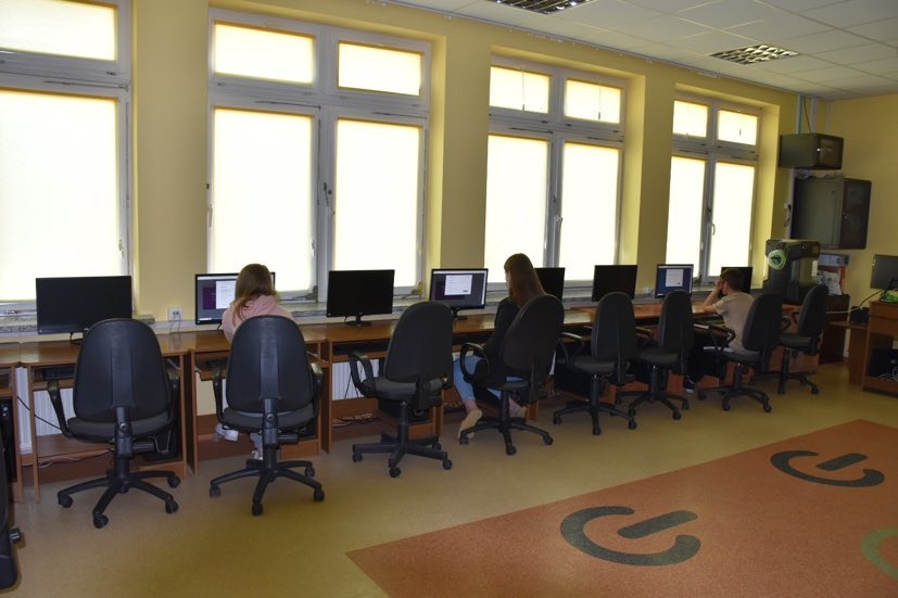Uczniowie przy stanowiskach komputerowych w pracowni informatycznej wypełniają test konkursowy