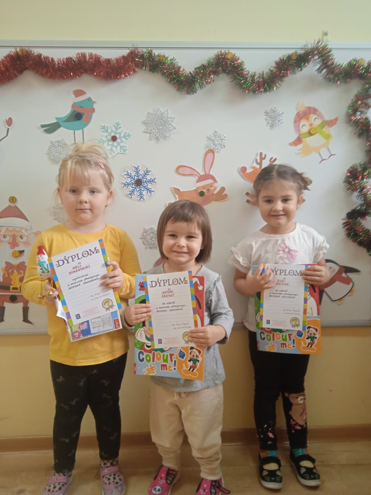 Dzieci z grupy "Poziomki" trzymają w rękach otrzymane dyplomy i nagrody za udział w konkursie plastycznym "Bombka choinkowa". 