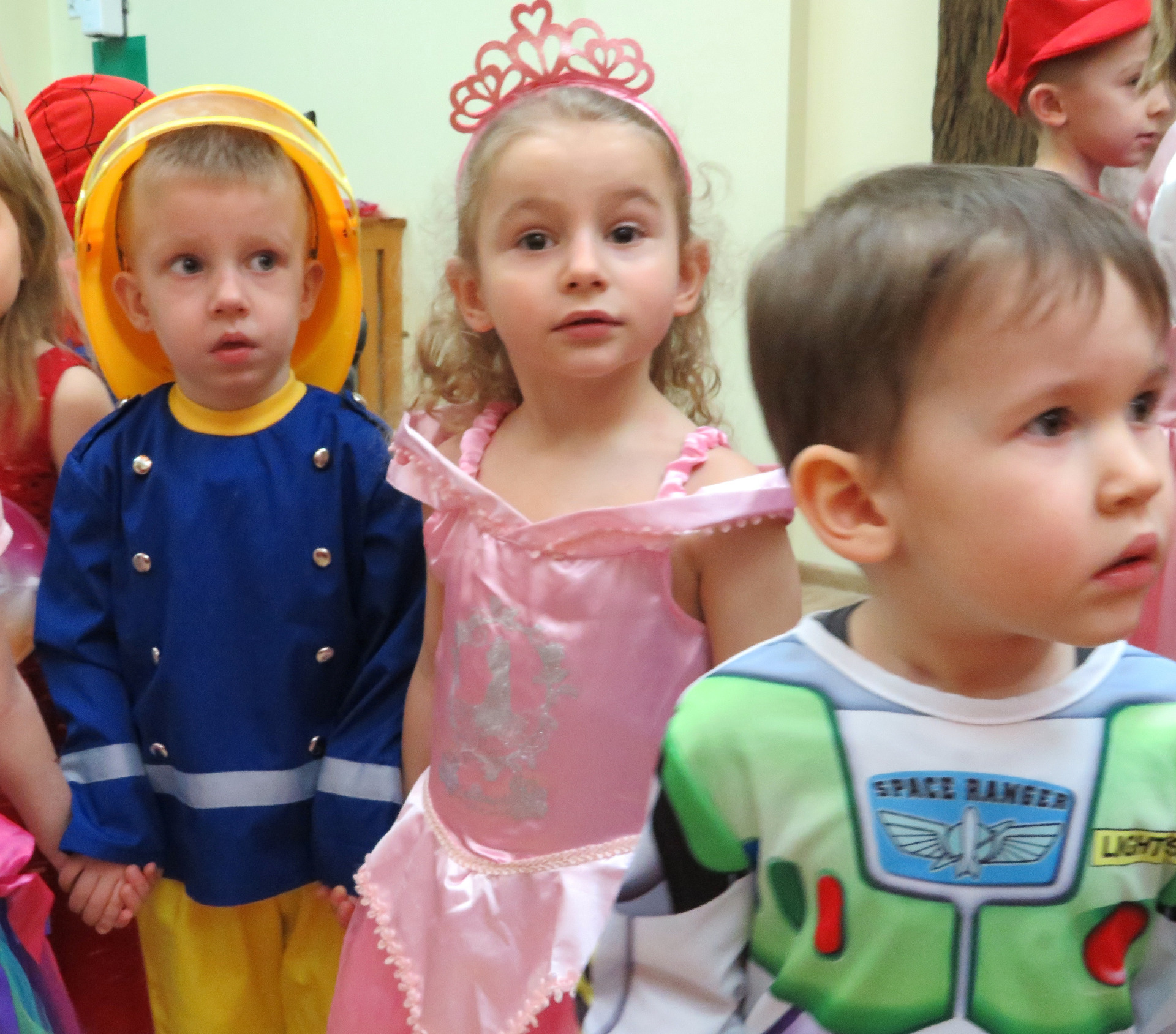 Troje dzieci z najmłodszej grupy w strojach strażaka, księżniczki i robota podczas balu karnawałowego.