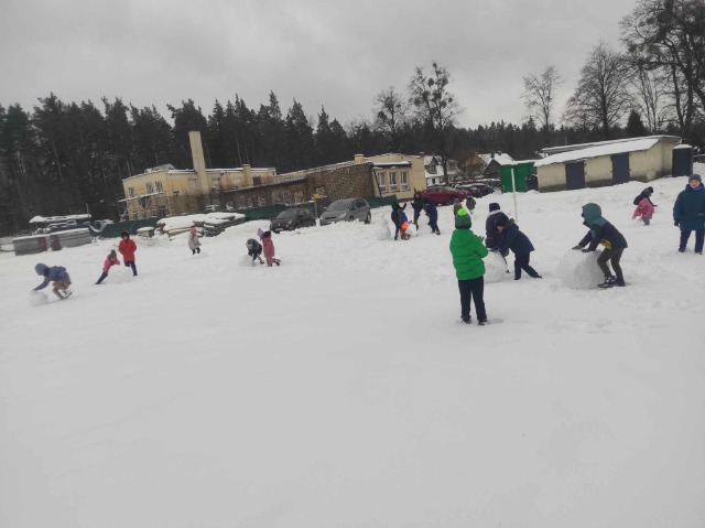 w oddali budynek szkoły, dzieci bawią się na śniegu, lepiąc kule